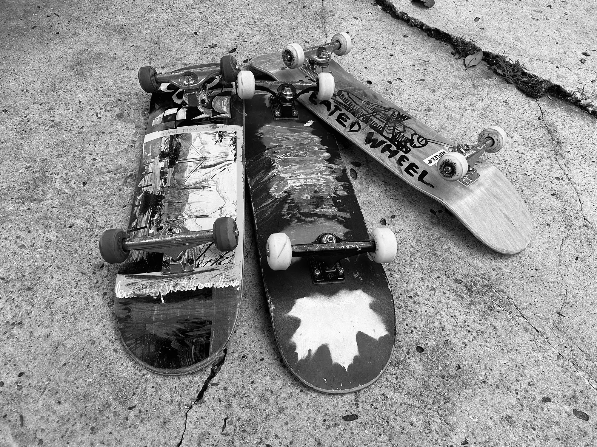 Three skateboards lying on cracked pavement, wheels up